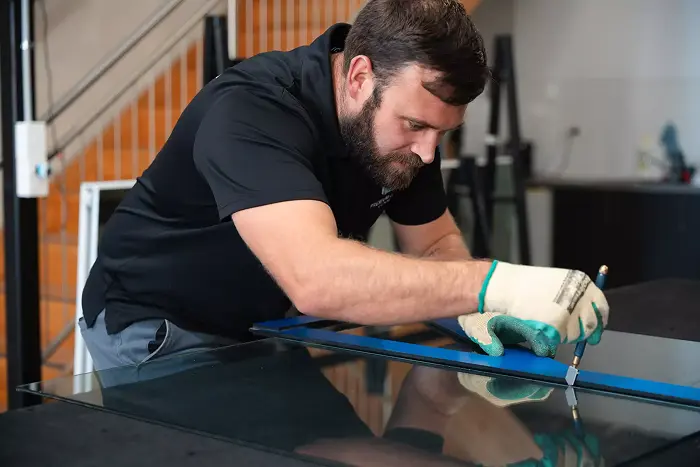 Glazier cutting a glass sheet to precise dimensions during a repair or replacement service.