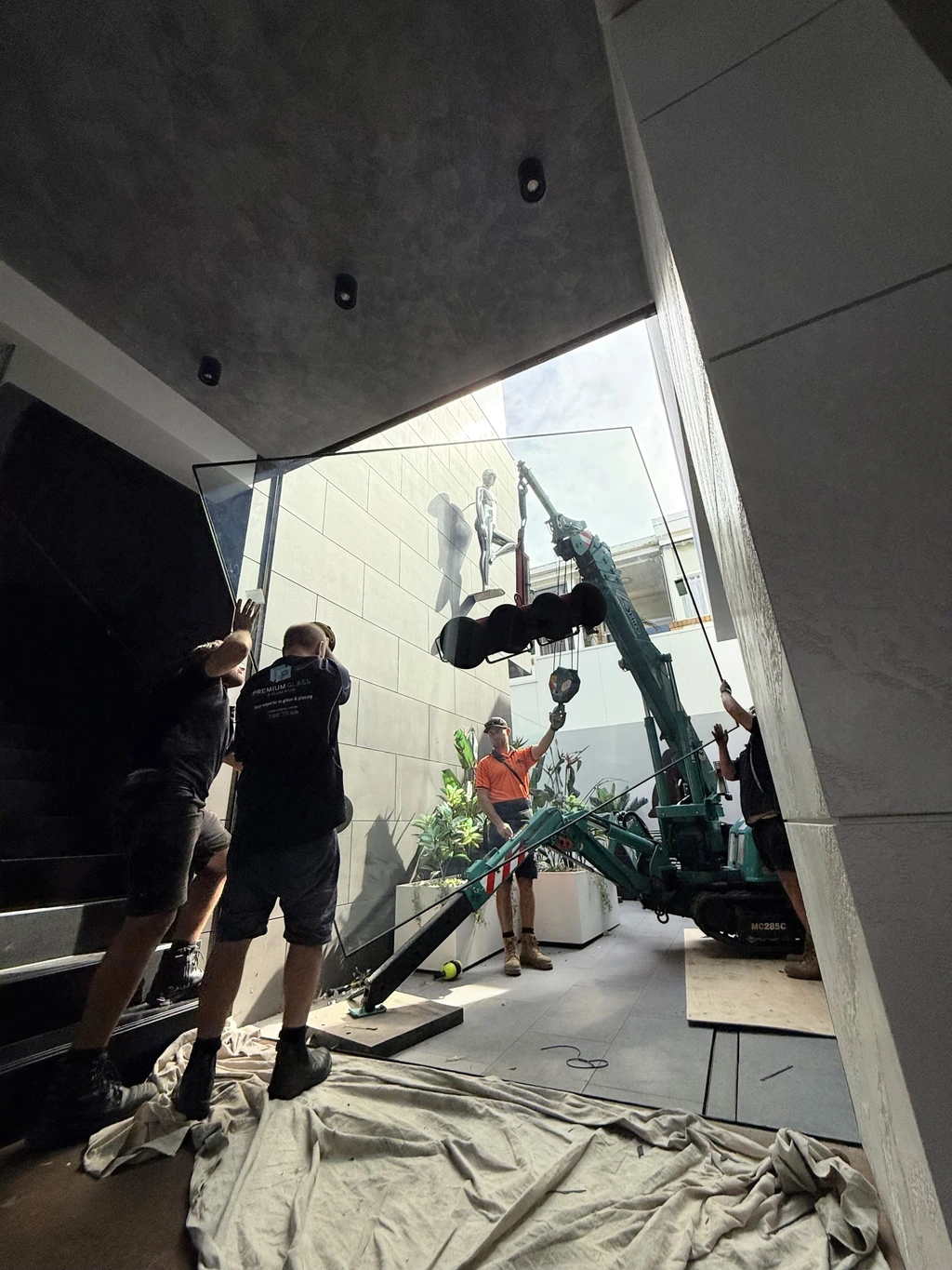 Team of glaziers in Melbourne using a mini crane to install a large glass panel inside a modern building stairwell.