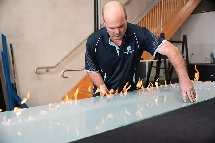 Glazier performing precision flame work on glass, showcasing advanced techniques in repair and finishing.